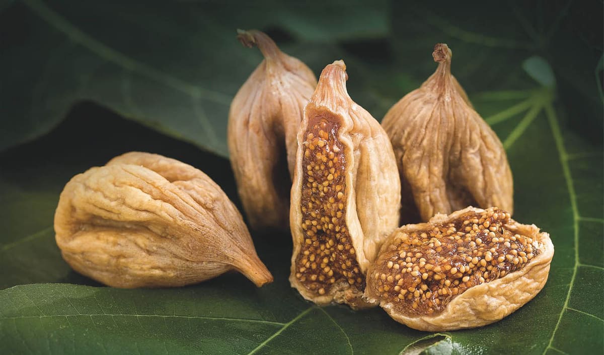 Whole and halved dried figs resting on a green fig leaf